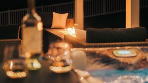 A cozy outdoor seating area with a hot tub, a bottle, and candles. - Lion’s Lookout | PSU Retreat w/Hot Tub & Game Room (Bellefonte)