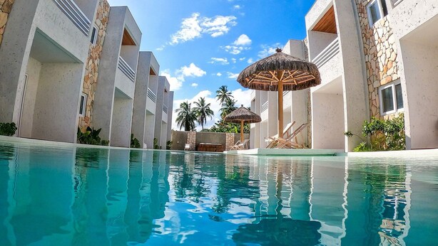 Zona de piscina con agua azul cristalina, rodeada de edificios modernos con fachadas de piedra y detalles de madera.