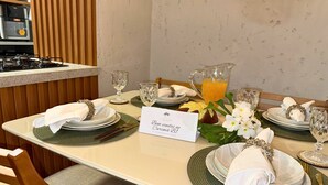 Mesa de comedor servida con platos, vasos y una jofaina de jugo de naranja, con un cartel que anuncia un menú especial de desayuno.