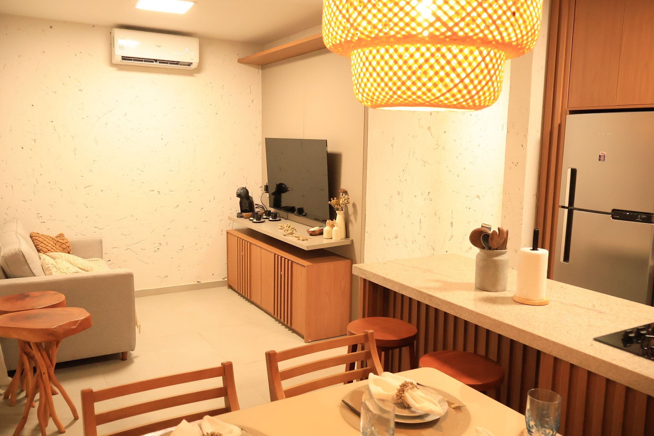 Una cocina compacta con horno integrado, un comedor con mesa y sillas de madera, una pequeña barra y un ventanal grande.