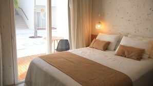 Habitación de hotel con cama, mesita de noche, lámpara, silla y vista a una escalera y zona exterior.