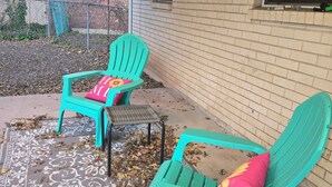 Un patio con dos sillas Adirondack turquesa, un tapete estampado y una pared de ladrillo.