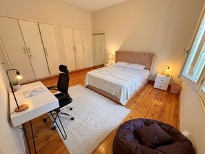 Une chambre à coucher avec un lit, un bureau, une chaise, une table de chevet et une fenêtre.