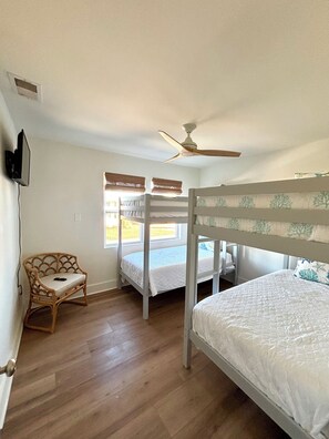 Ein Zimmer mit Etagenbetten, einem Deckenventilator, einem Stuhl und einem Fenster mit Jalousien.