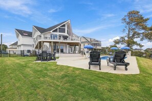 Ein zweistöckiges Haus mit überdachter Terrasse, Sitzgelegenheiten im Freien und einem Swimmingpool.