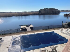 Une piscine dotée d’une terrasse, entourée d’une clôture, et offrant une vue sur un lac paisible où sont amarrés des bateaux à proximité.
