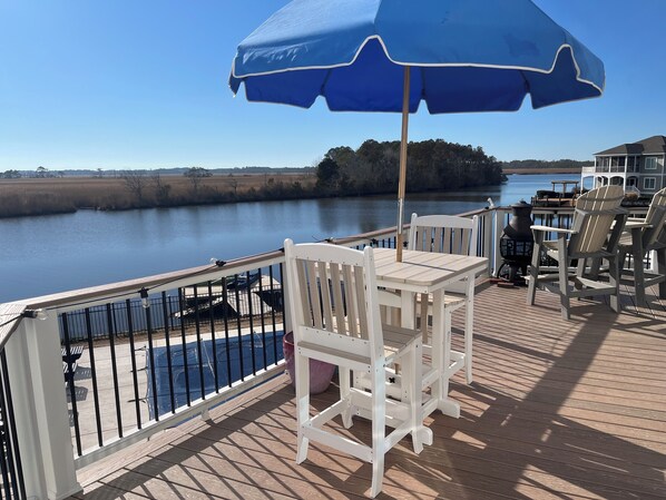 Une terrasse avec une table et des chaises, offrant une vue sur une étendue d’eau calme et une côte lointaine.