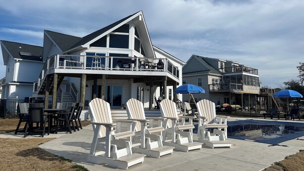 A two-story house with a balcony, outdoor seating area with Adirondack chairs, and a pool. - Waterfront Bay Views, Private Pool, 6 Bedroom, Pet-Friendly! Sleeps14 (Virginia Beach)