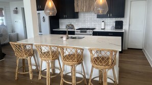 A modern kitchen with dark cabinets, a white island with bar stools, and pendant lighting. - Waterfront Bay Views, Private Pool, 6 Bedroom, Pet-Friendly! Sleeps14 (Virginia Beach)
