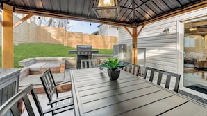 En udendørs terrasse med et bord, stole, grill og en potteplante.