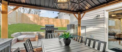 An outdoor patio with a table and chairs, a grill, and a potted plant.