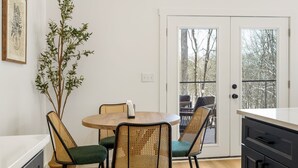 Un comedor con una mesa redonda, cuatro sillas de mimbre, una planta en maceta y vistas a una terraza exterior a través de un ventanal.