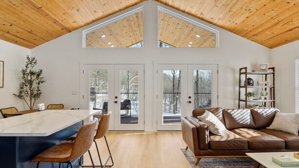 Un amplio salón con techo alto, una gran mesa de comedor de madera y un cómodo sofá marrón.