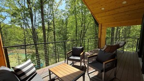 Una terraza de madera con mobiliario exterior, vista a un bosque y barandilla metálica.