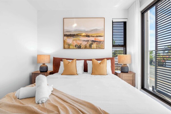Une chambre d’hôtel avec un grand lit, deux lampes de chevet, un tableau au-dessus du lit et une fenêtre avec des stores.