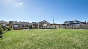 A residential backyard with a covered patio, a brick house, and a wooden fence. - Great home for families and groups (Culburra Beach)