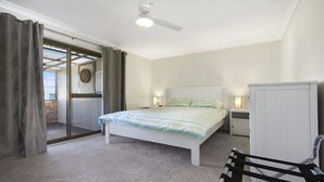 Un dormitorio con una cama, un ventilador de techo, un armario y una puerta que da a un balcón.