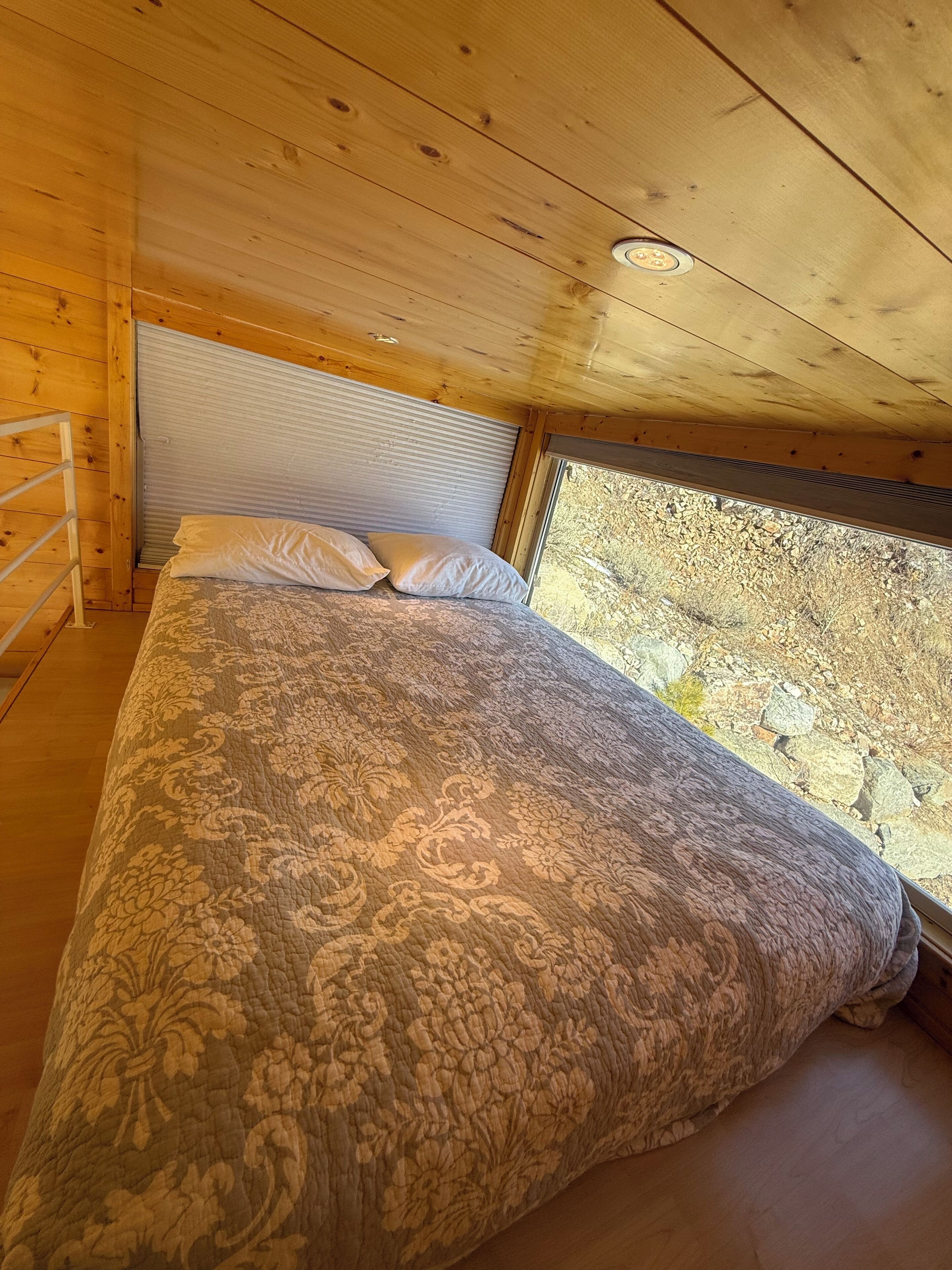A bedroom with a bed, pillows, and a window with a view of a rocky landscape.