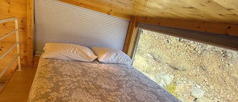 A bedroom with a bed, pillows, and a window with a view of a rocky landscape.