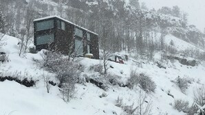 Een modern gebouw met twee verdiepingen en grote ramen, omgeven door met sneeuw bedekte bomen en een helling.