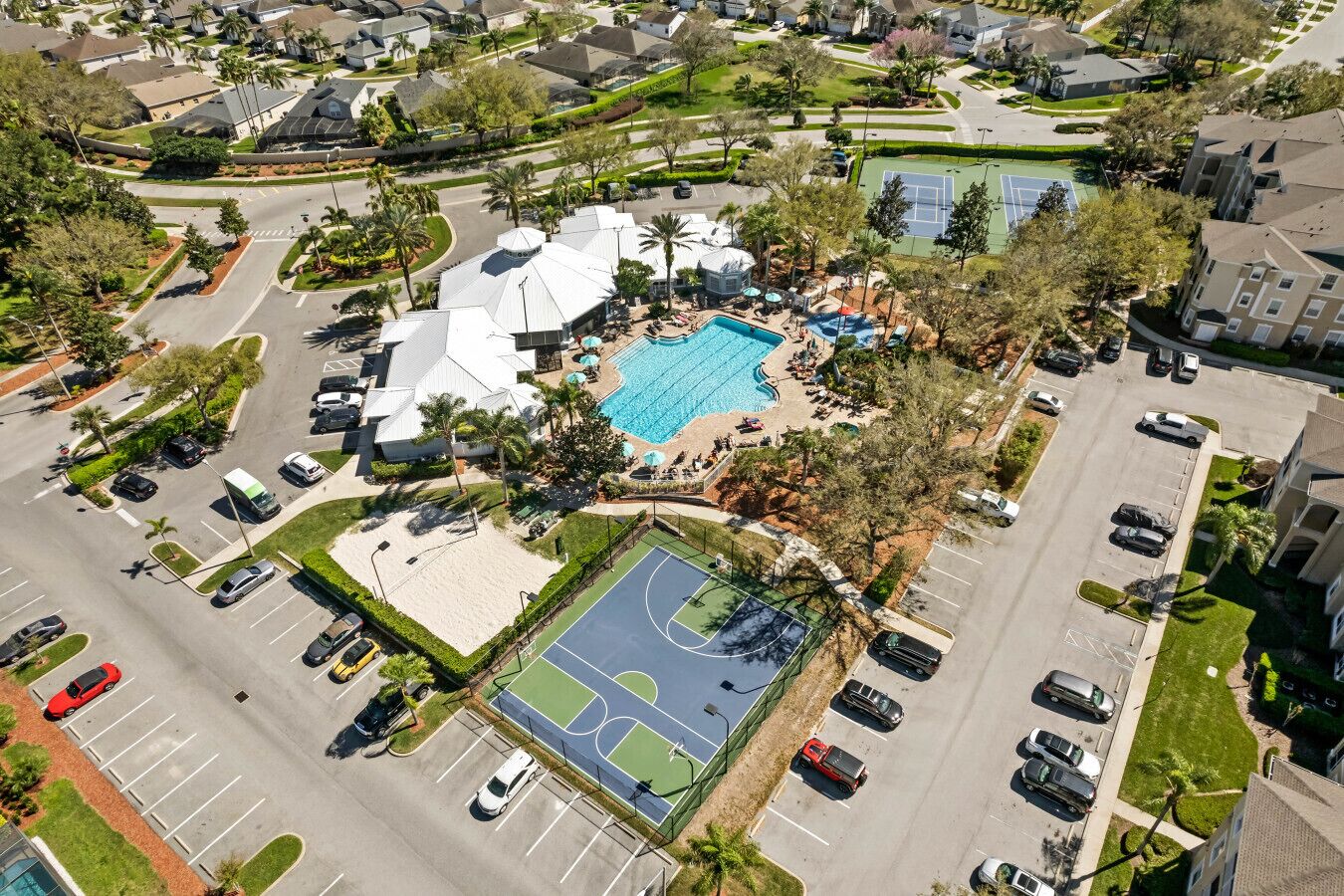 An aerial view of a residential area with a swimming pool, tennis courts, and a parking lot.