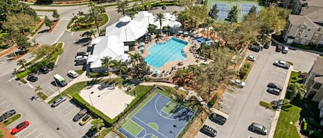 An aerial view of a residential area with a swimming pool, tennis courts, and a parking lot.