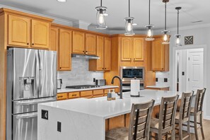 A modern kitchen with wooden cabinets, stainless steel appliances, a marble island, and pendant lighting. - Copper Cove! Hot Tub, 5 Kings & 6 Bunks. FirePit-Sunroom-Sundeck-kayaks-SUP-Fish (Bracey)