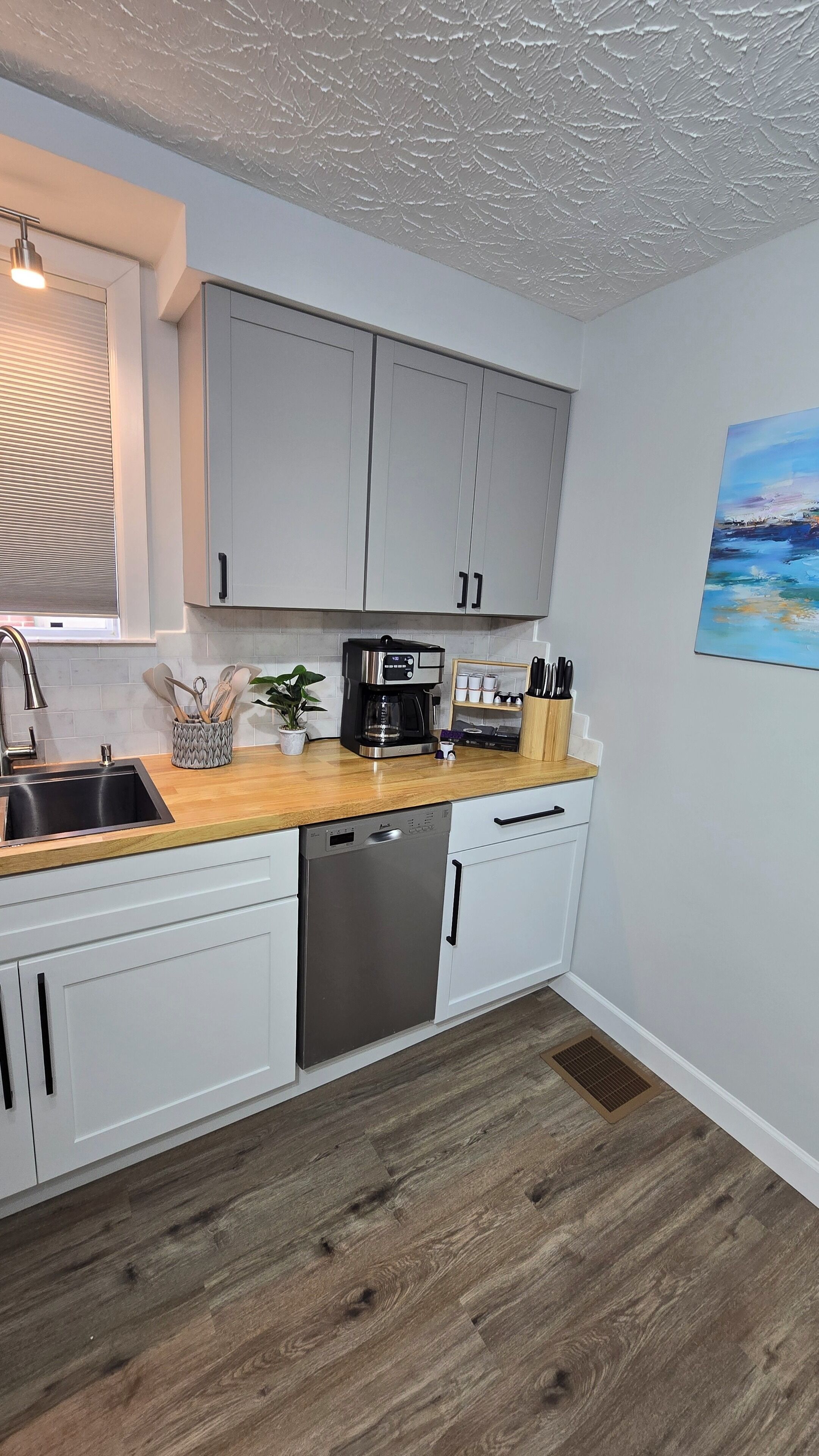 A modern kitchen with white cabinets, a stainless steel dishwasher, and a wooden countertop.
