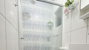 Ein modernes Badezimmer mit Duschkabine aus Glas, weißen Fliesen, Toilette, Waschbecken mit Handtuch und einer kleinen Pflanze an der Wand.