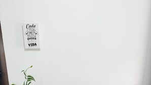 Ein modernes Wohnzimmer mit Flachbildfernseher auf weißem TV-Schrank, einem Blumentopf, einem gerahmten Motivationsspruch an der Wand und einem gemusterten Teppich.