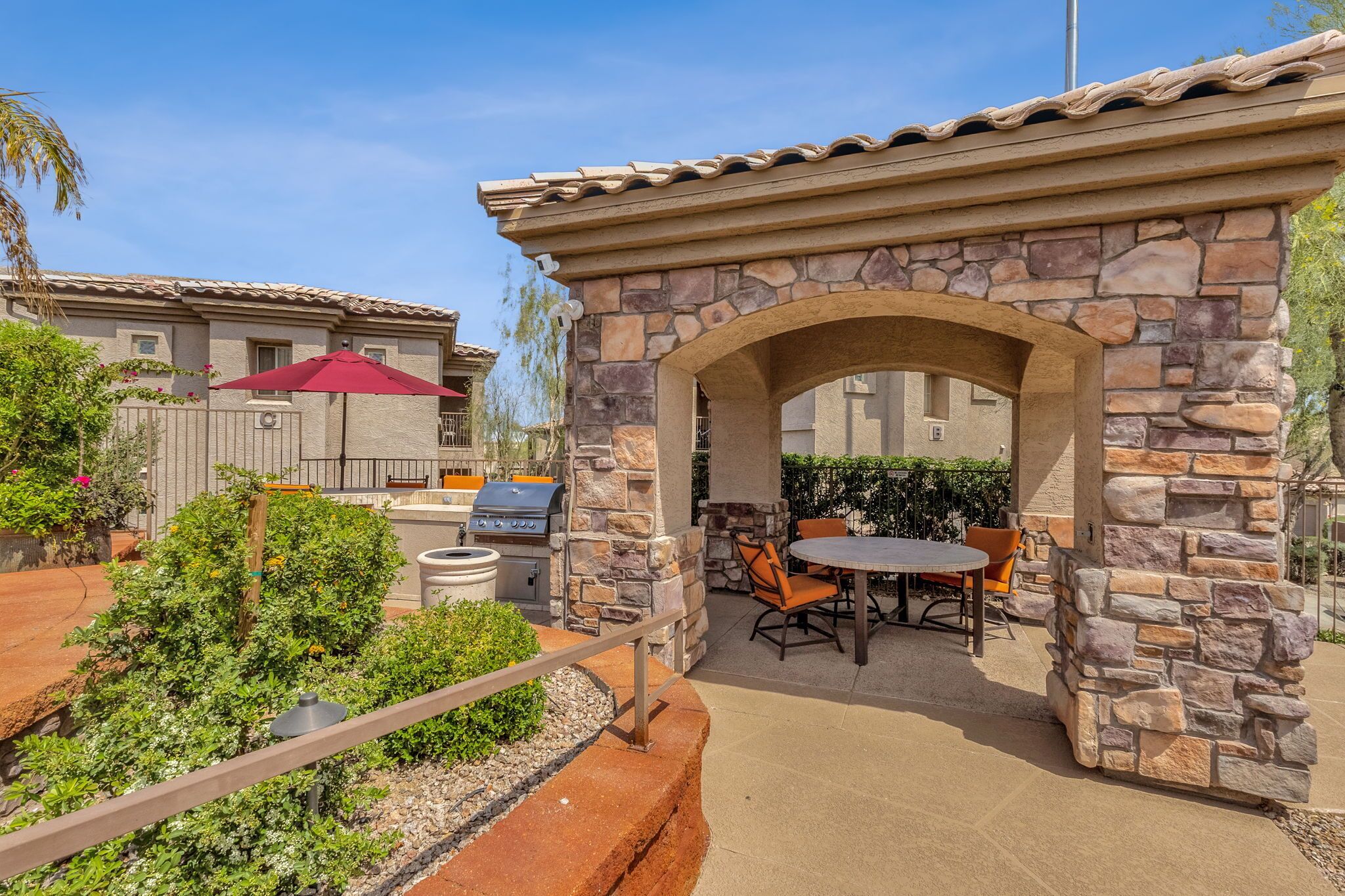 An outdoor patio area with stone walls, a barbecue grill, and a dining table with chairs.