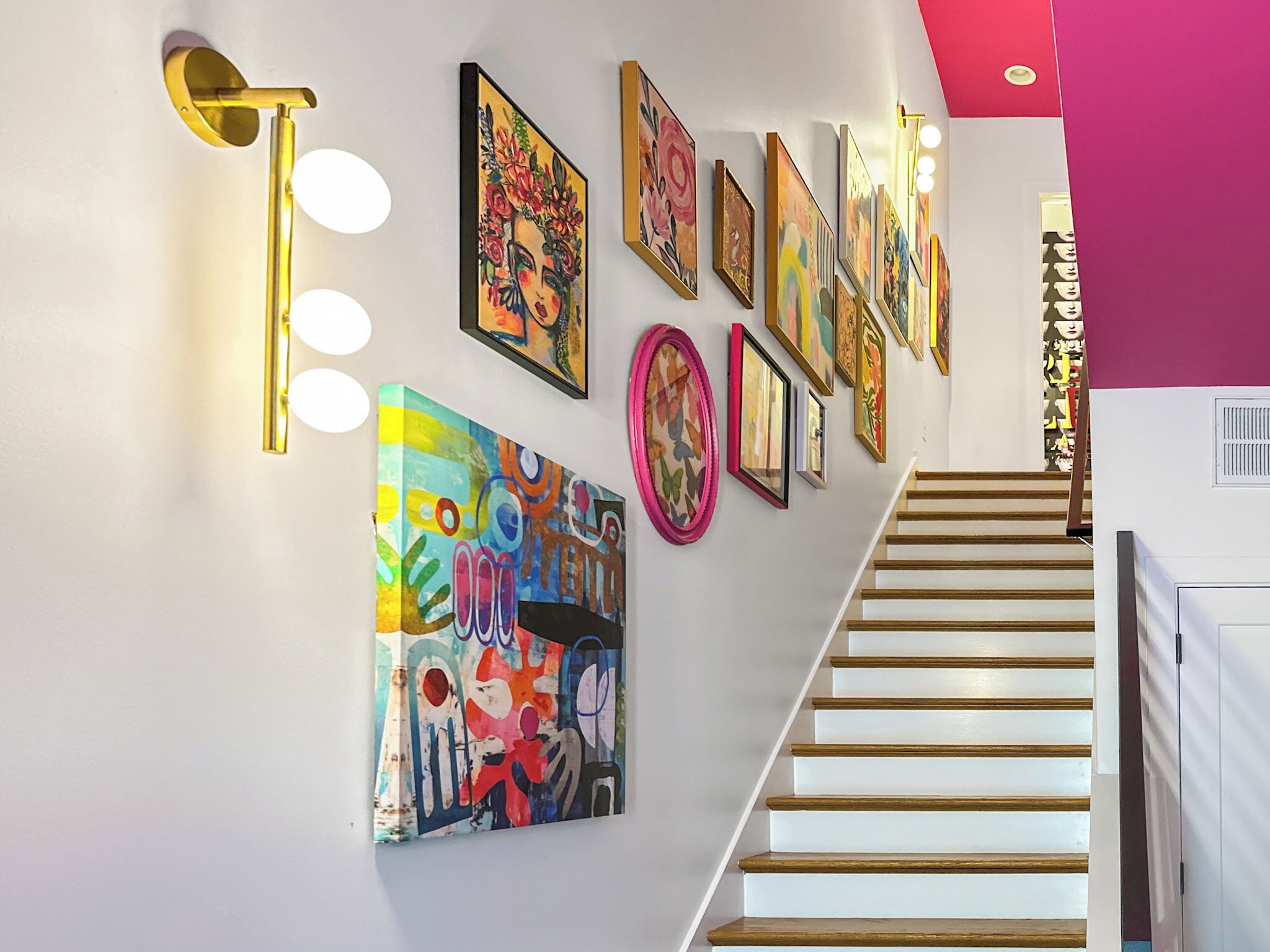 A staircase with a white railing, surrounded by various framed artworks on the walls.