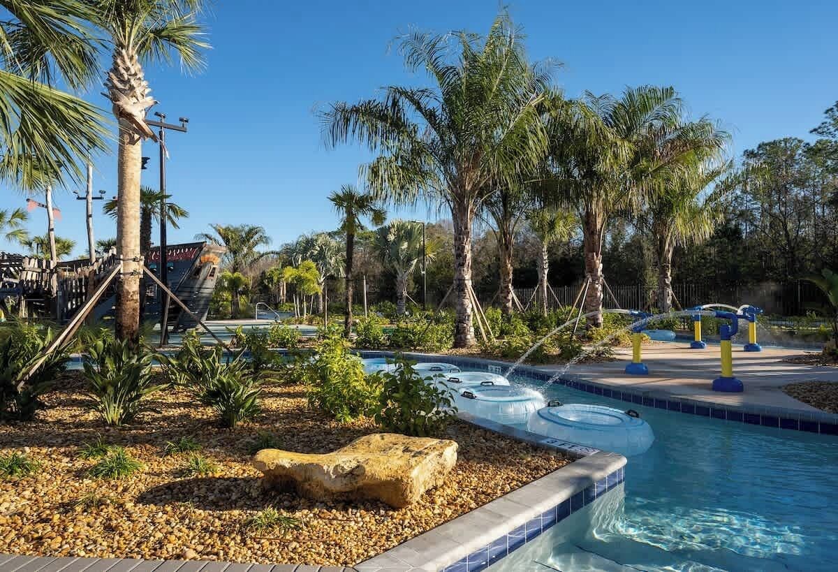 Zona de piscina con palmeras, una formación rocosa y toboganes de agua.