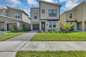 A modern two-story residential building with a garage, a well-maintained lawn, and a paved driveway. - Classy 6BR Home With Private Pool (Kissimmee)