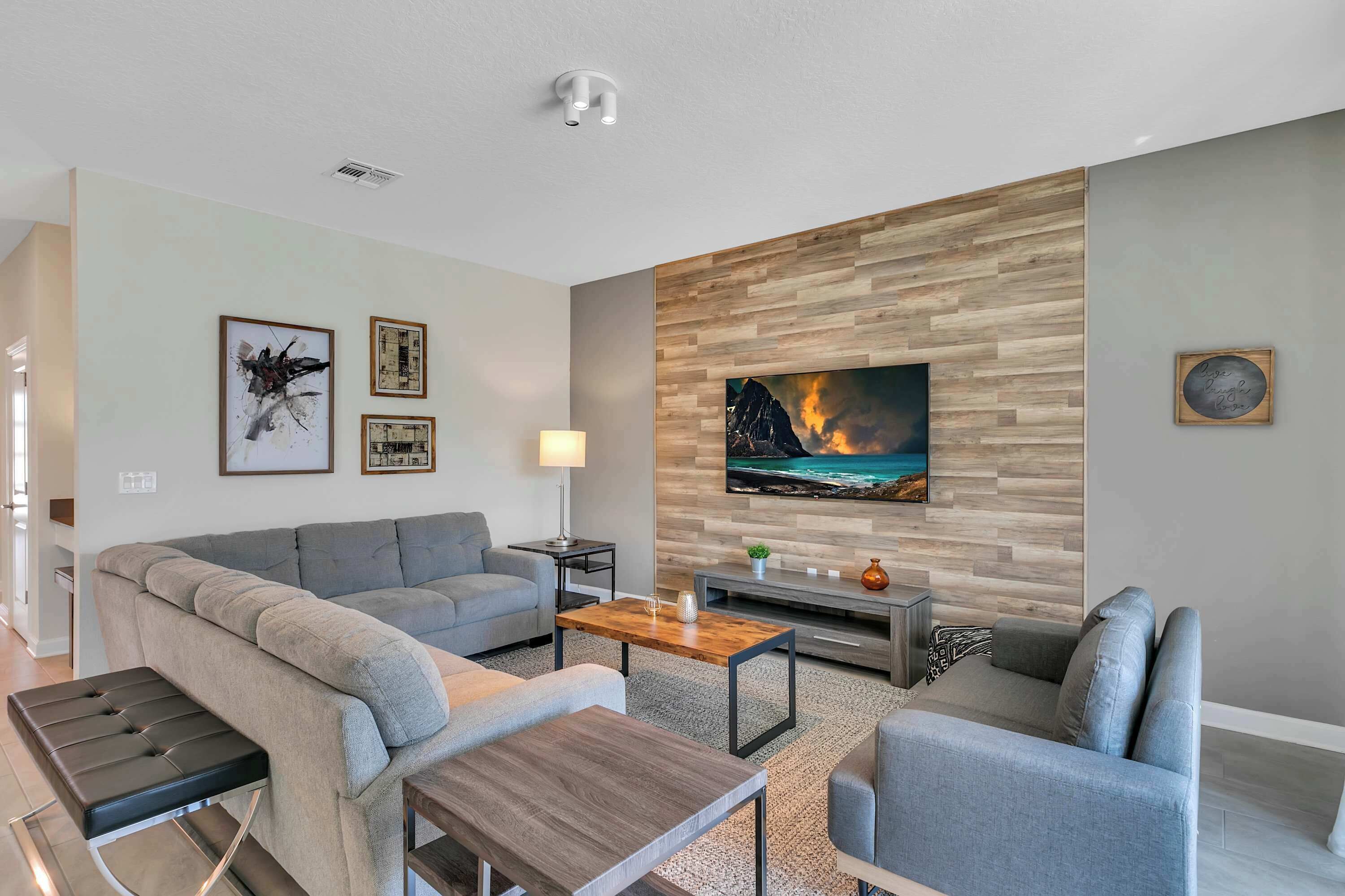 A modern living room with a grey sofa, a wooden coffee table, and a flat-screen TV mounted on a wooden wall.
