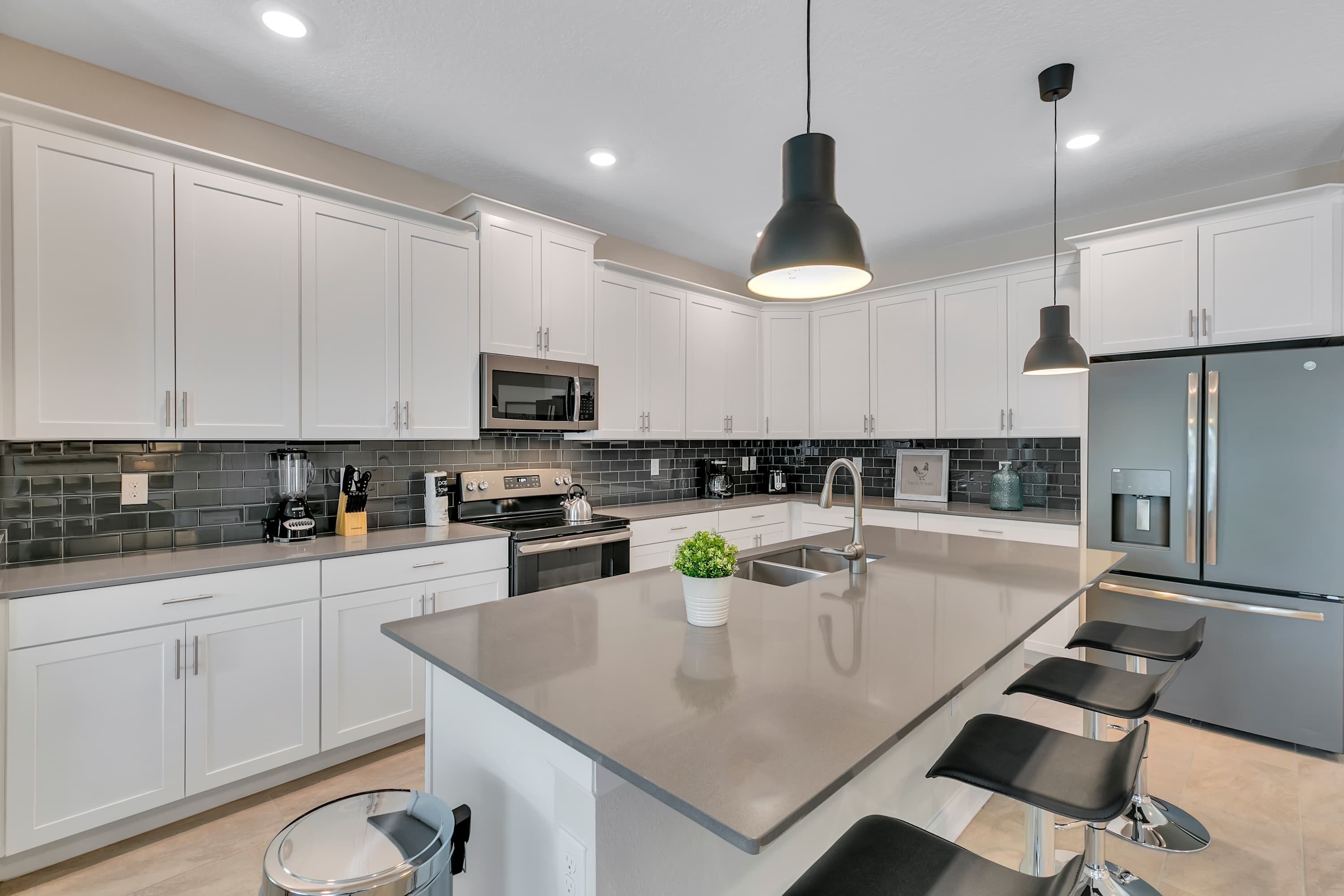 A modern kitchen with white cabinets, a central island with bar stools, a built-in microwave, and a stainless steel refrigerator.