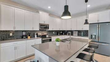 A modern kitchen with white cabinets, a central island with bar stools, a built-in microwave, and a stainless steel refrigerator.