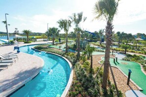 A swimming pool with a curved edge, surrounded by palm trees and a green play area. - Classy 6BR Home With Private Pool (Kissimmee)