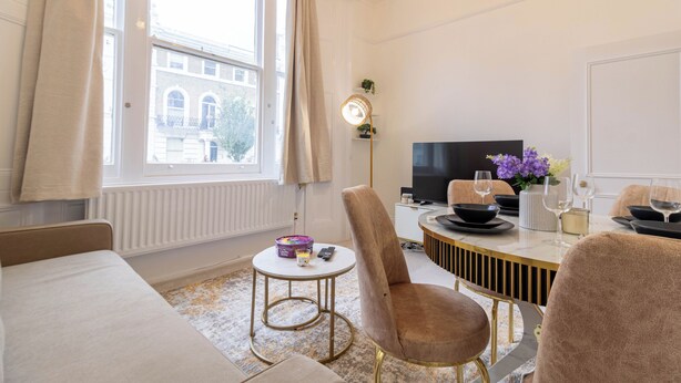 Moderni hotellihuone, jossa on suuri ikkuna, sohva, ruokapöytä tuoleineen ja televisio.