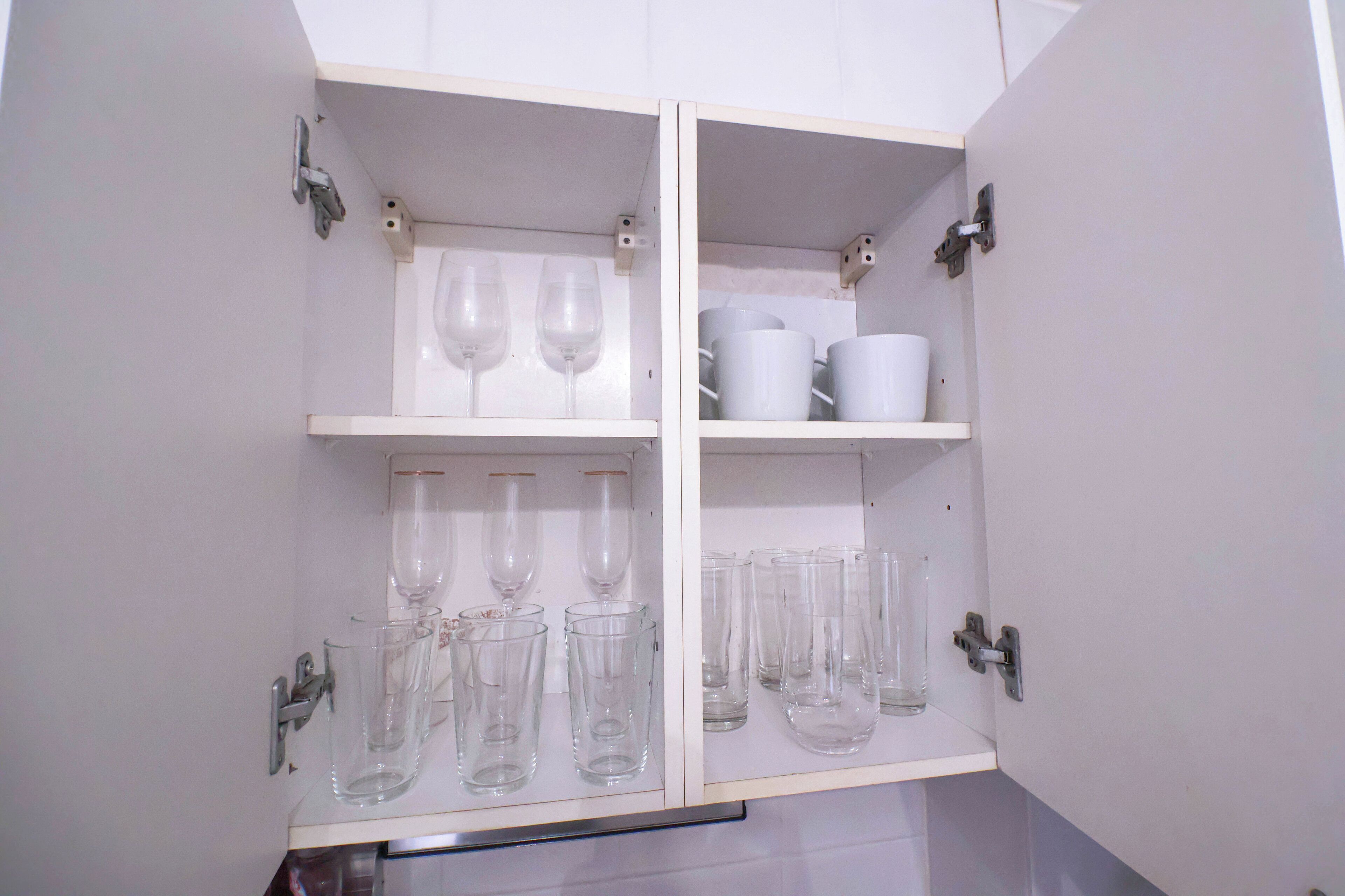Un meuble blanc doté de plusieurs étagères, contenant des verres transparents et des tasses blanches.