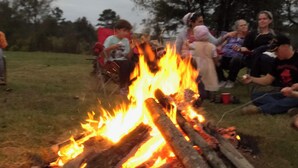Eine Gruppe von Menschen versammelt sich um ein Lagerfeuer in der freien Natur.