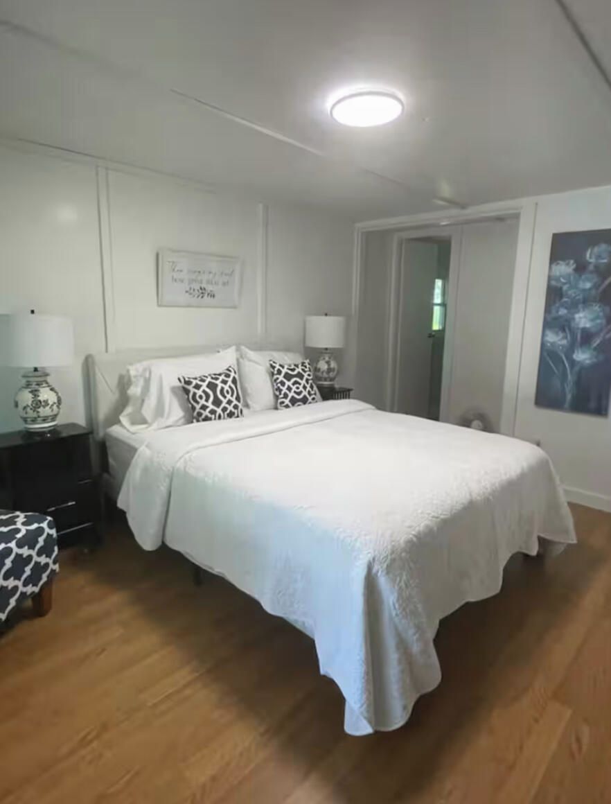 A bedroom with a bed, nightstands, a lamp, a chair, a door, and a wall with a framed picture.