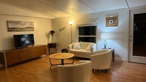 Ein Wohnzimmer mit einer Couch, Sesseln, einem Couchtisch, einem Fernseher und einer Lampe.