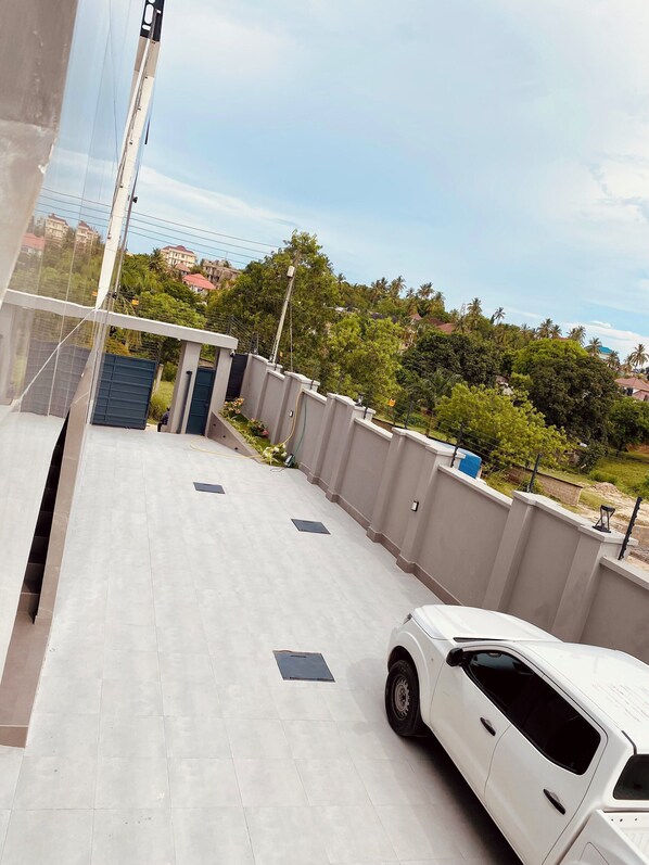 A white car parked on a tiled rooftop with a view of a residential area and trees in the background. - Fahari Suites By WW (Dar es Salaam)