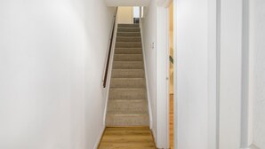 Un estrecho pasillo con una escalera empapelada que conduce a una habitación con piso de madera.