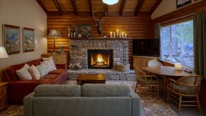 Una sala de estar acogedora con chimenea de piedra, vigas de madera, un televisor y un ventanal grande.