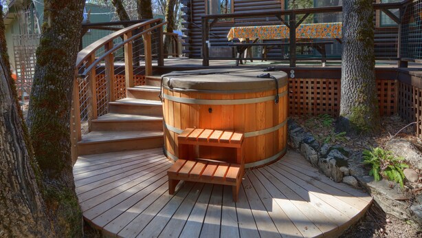 Una terraza de madera con un jacuzzi, escalones de madera y una mesa con mantel estampado.