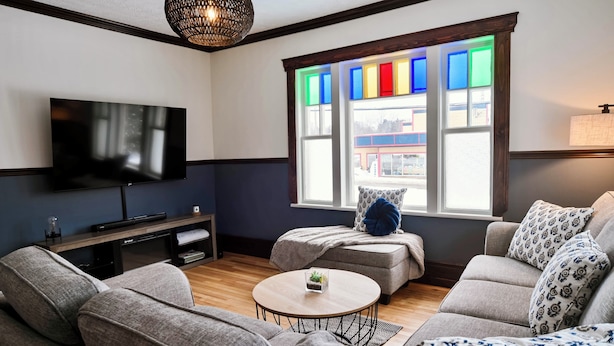 A living room with a flat-screen TV, a sofa, a coffee table, and a window with colorful panes.