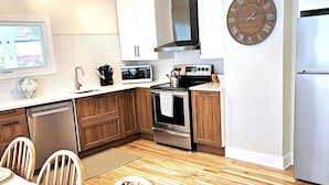 A modern kitchen with wooden cabinets, stainless steel appliances, a microwave, and a clock on the wall.