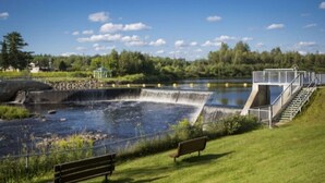 A dam with a water spillway, a bench, and a gazebo in a park setting.